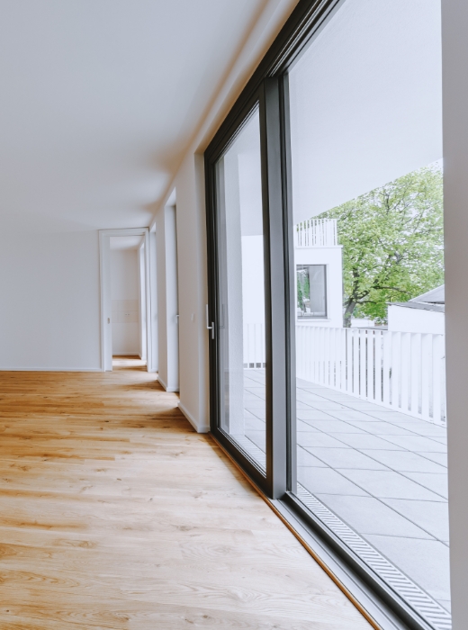Der Balkon ist durch eine Schiebetür und bodentiefe Fenster mit dem Wohnzimmer verbunden.